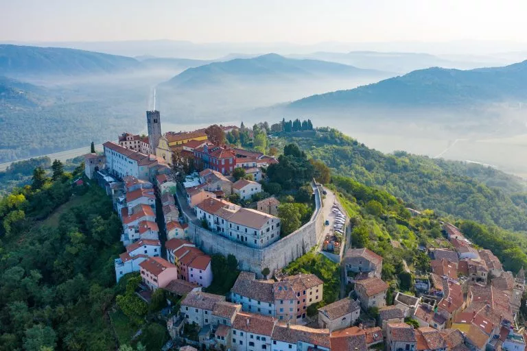 Antike Stadt Motovun auf dem Gipfel des Berges, umgeben von einer Festungsmauer, im Hintergrund Berge und Nebel am Fuße der Berge. Istrien, Kroatien: Der Blick aus der Drohne.