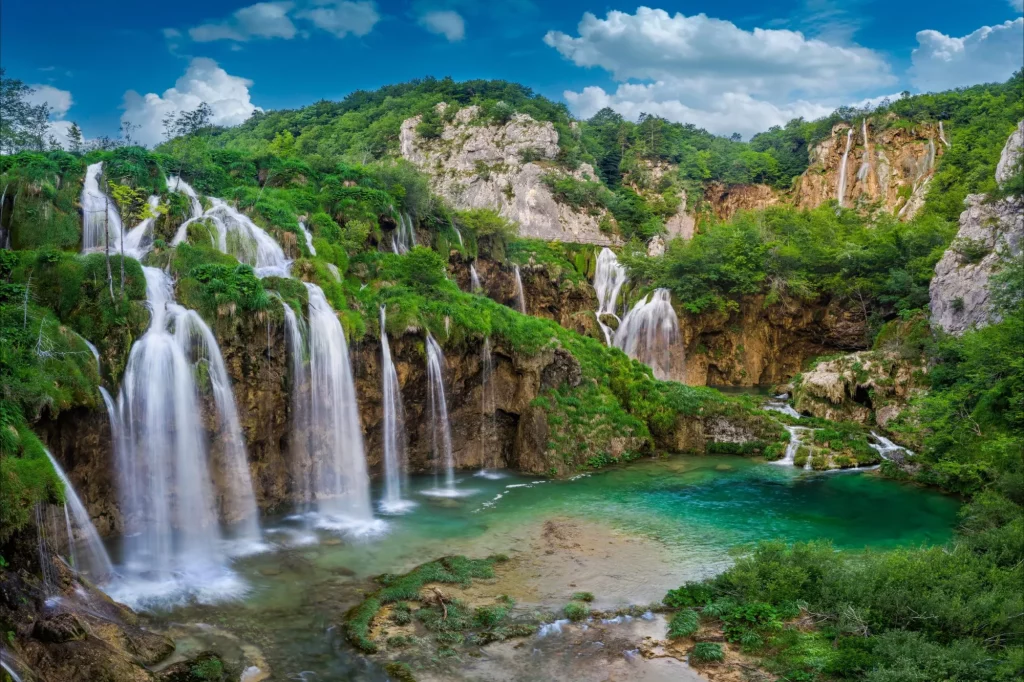 Plitvice, Croatia - Beautiful waterfalls of Plitvice Lakes (Plitvička jezera) in Plitvice National Park on a bright summer day with blue sky and clouds and green foliage and turquise water